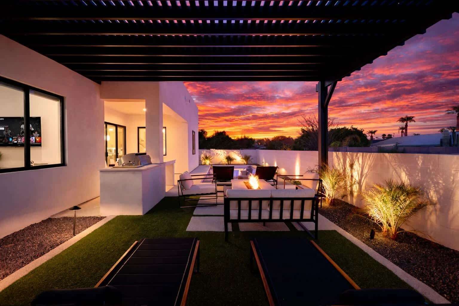 A modern outdoor patio with a fire feature, seating, and a view of a sunset.