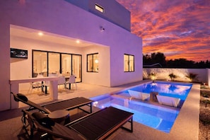 Una casa moderna con piscina, mobiliario exterior y televisor montado en la pared.