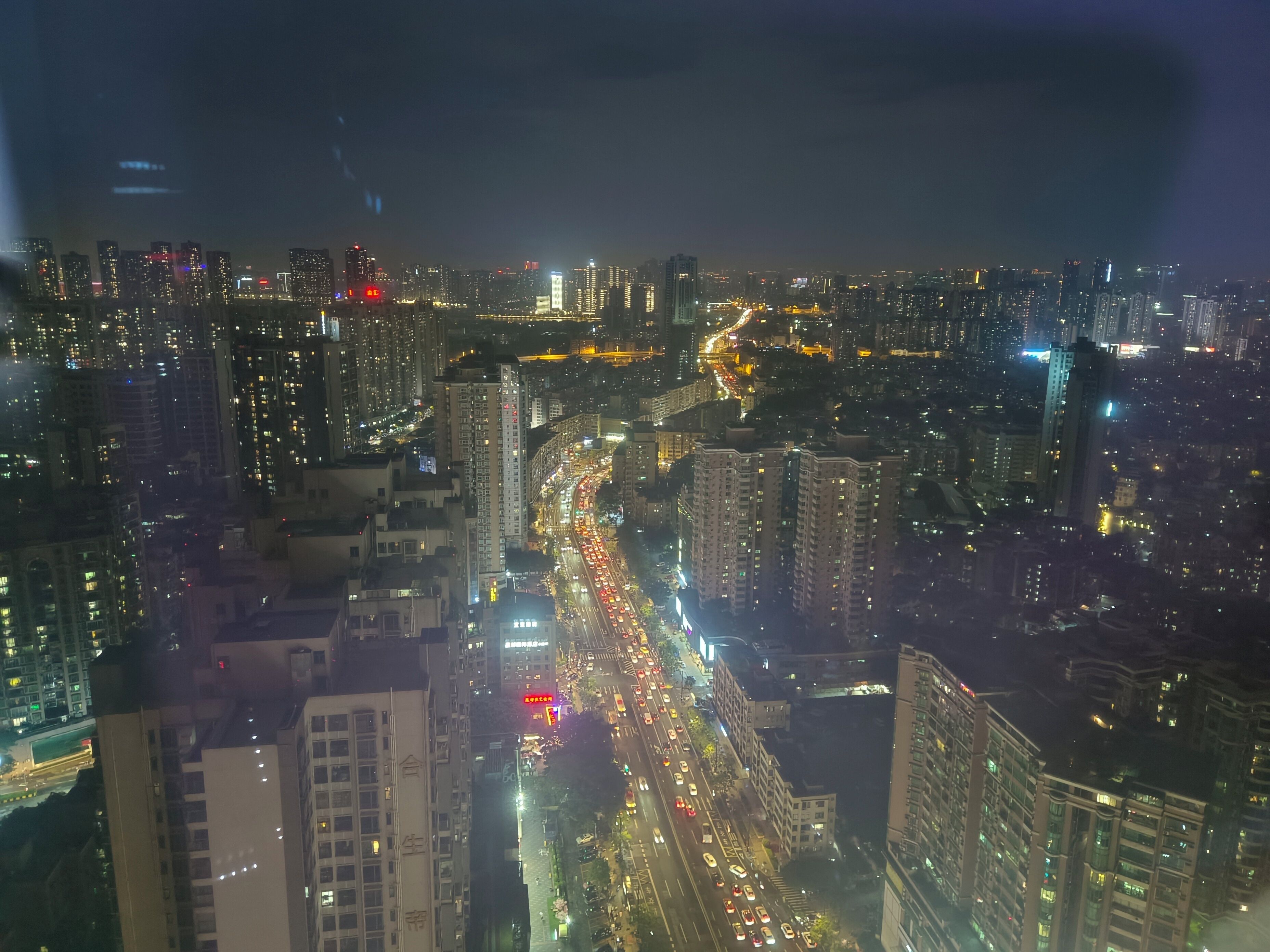 A nighttime cityscape with high-rise buildings, busy streets, and illuminated signs.