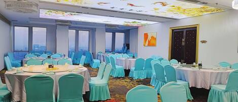 A conference room with round tables, teal chairs, and a city view through large windows.