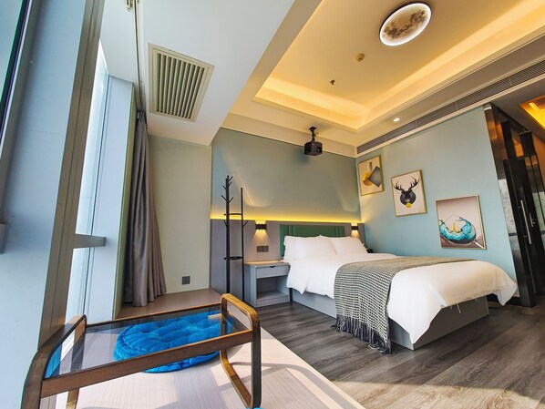 A modern hotel room with a large bed, a bedside table, a nightstand, a desk, a chair, a small pool table, and a ceiling projector.