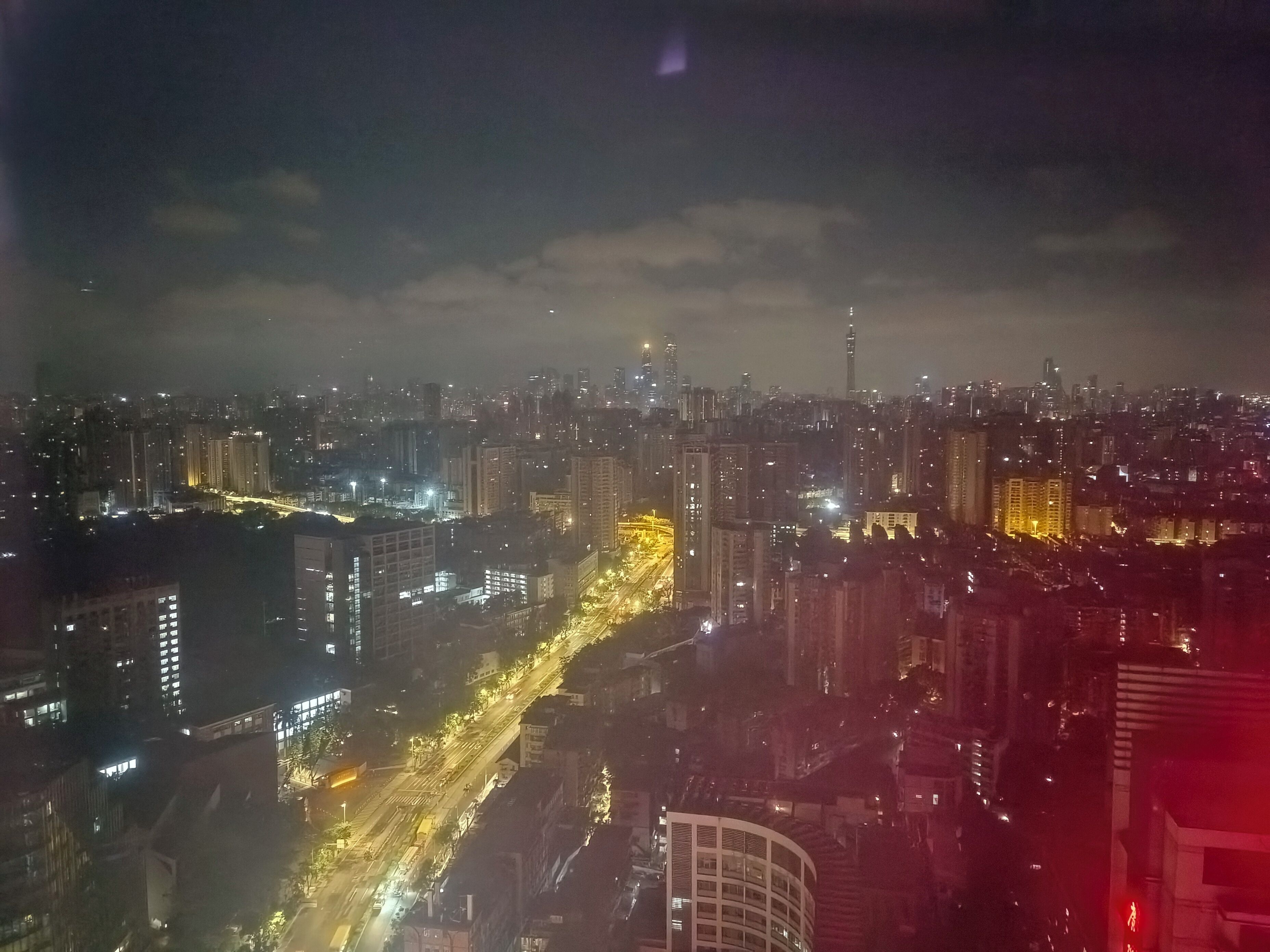 Une vue nocturne d’une ville, avec des bâtiments illuminés et une rue animée.