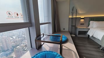 Ein modernes Hotelzimmer mit großem Fenster, einem Bett, einem Nachttisch, einer Lampe und einem blauen Sitzsack.