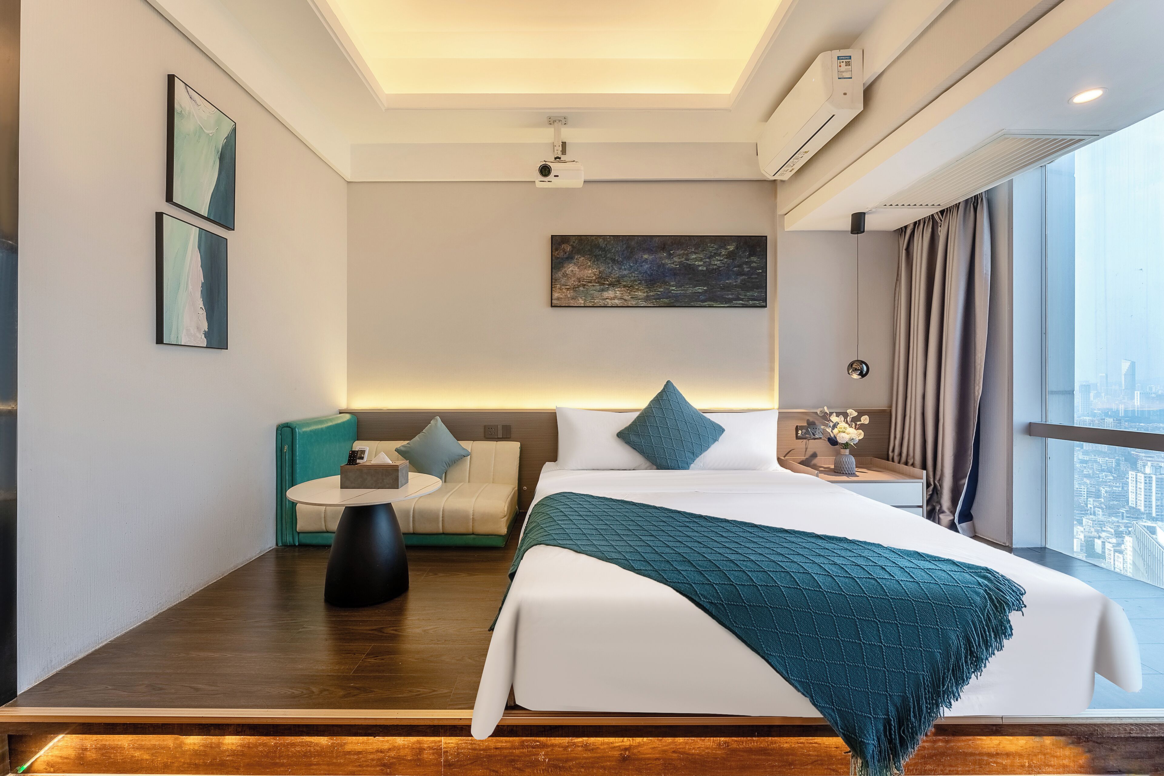 Quarto de hotel moderno com uma cama grande, um sofá, uma mesa pequena e vista para a cidade.