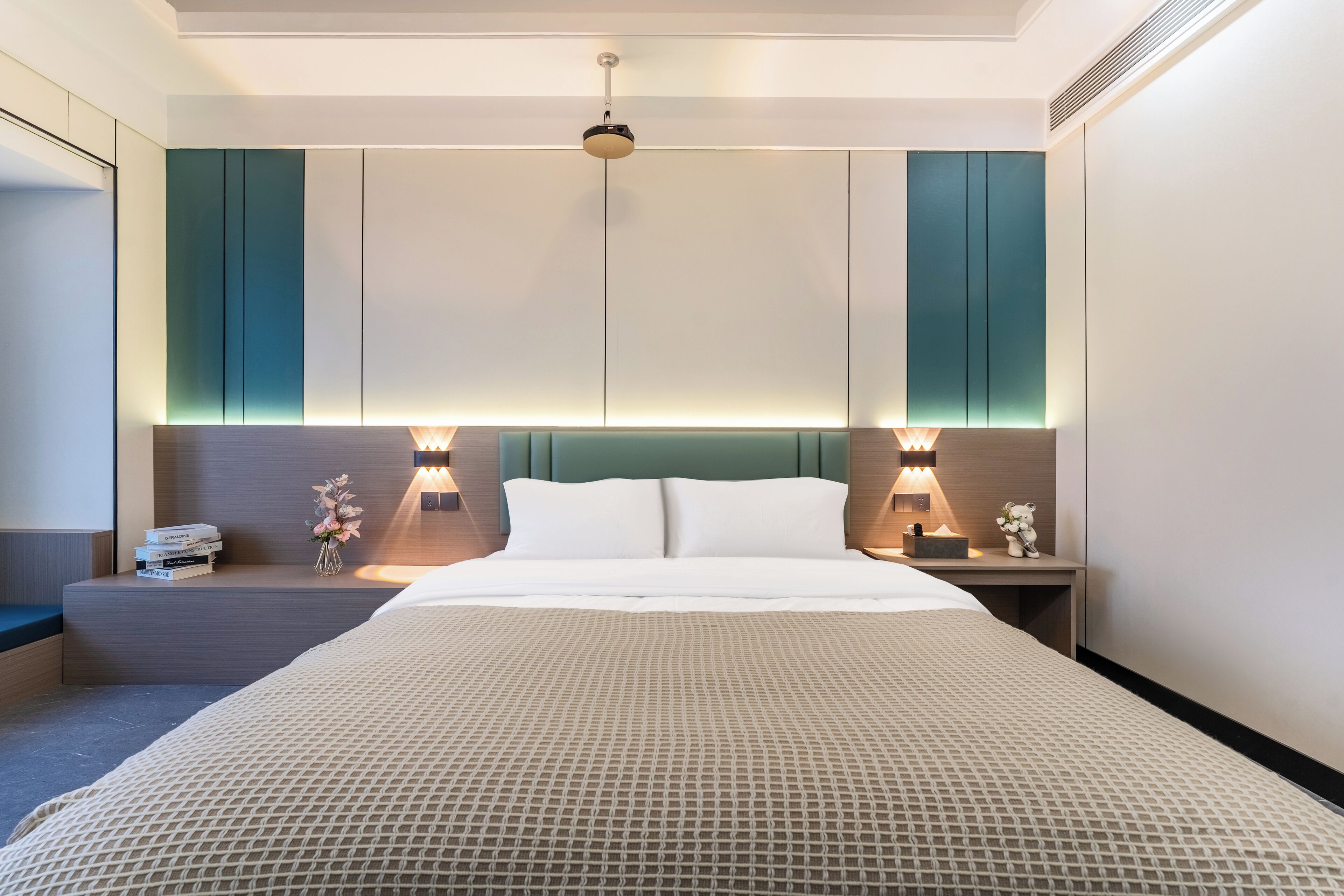 Een moderne hotelkamer met een groot bed, twee nachtkastjes met lampen, een bijzettafeltje en een zithoek met een bank.