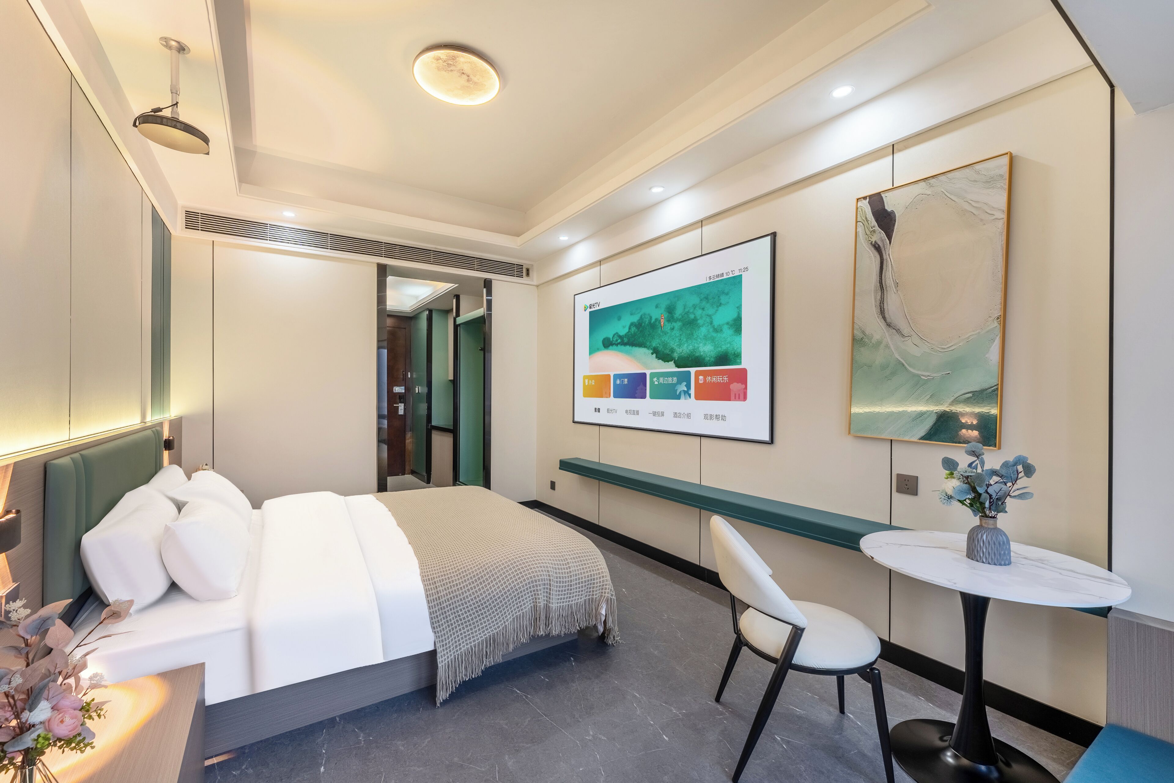 A modern hotel room with a bed, bedside table, chair, and artwork on the wall.