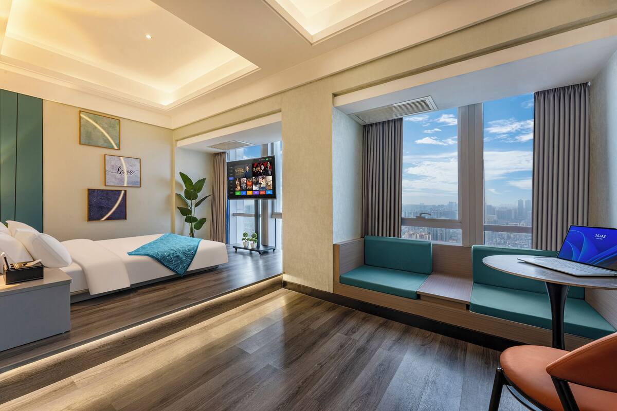 Habitación de hotel moderna con cama, zona de estar con una computadora portátil y un ventanal que ofrece vistas a la ciudad.