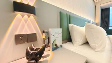 A hotel room with a bed, a bedside table with a game controller, a book titled 'Triangle Construction,' and a wall-mounted light fixture.