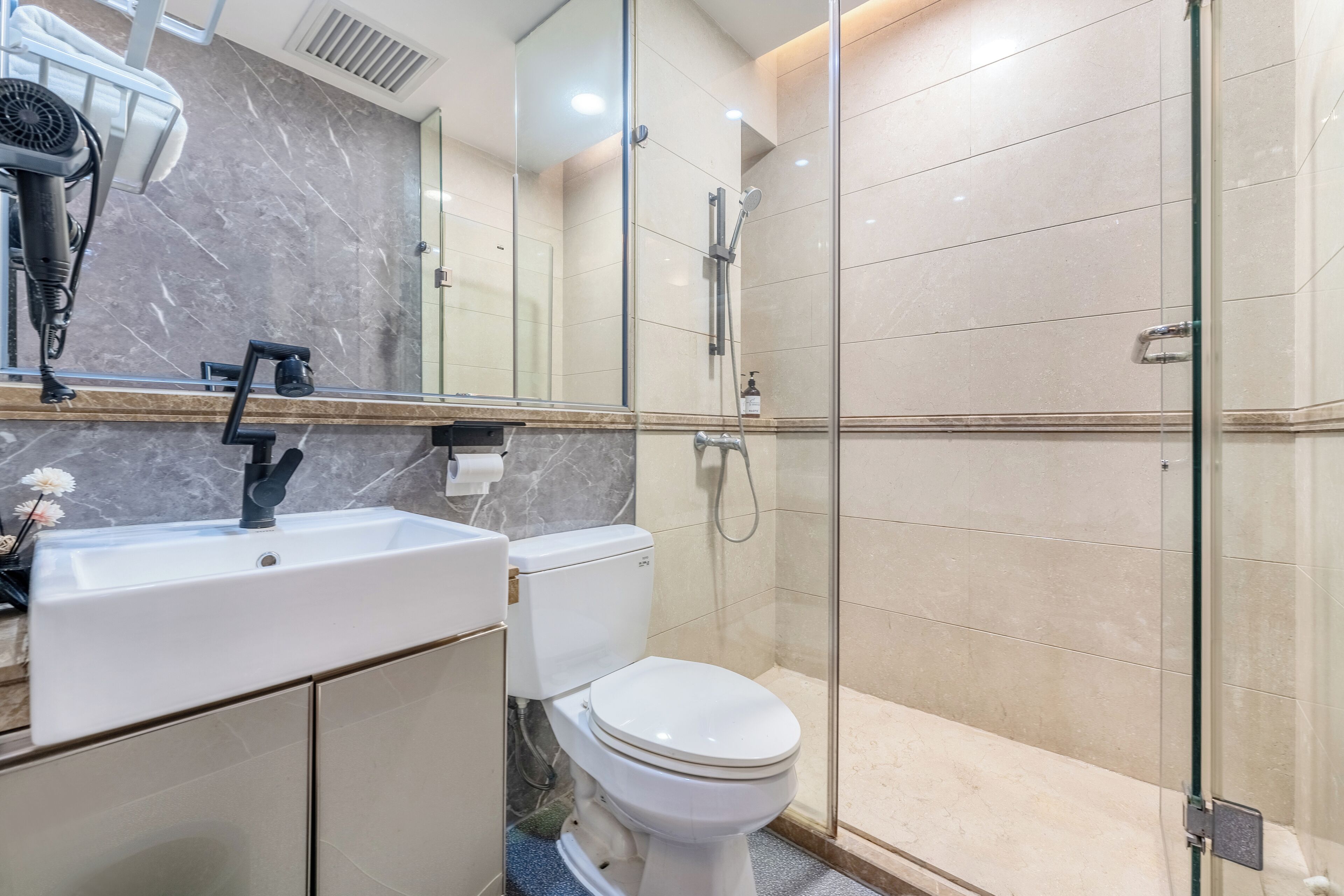 A modern bathroom with a marble sink, toilet, and glass-enclosed shower.