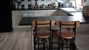 Une cuisine moderne avec des meubles blancs, un plan de travail noir et deux tabourets de bar en bois.