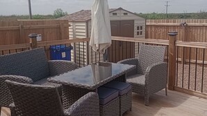A deck with wicker furniture and a table, surrounded by a wooden fence. - Lapwing Lodge, Howdales (Lincolnshire)
