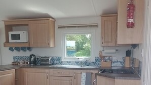 A compact kitchen with wooden cabinets, a microwave, a kettle, a toaster, and a gas stove. - Lapwing Lodge, Howdales (Lincolnshire)