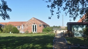 A brick house with a red roof, a front door, and a small garden area with a pathway leading to a table and chairs. - Wren Cottage, Howdales (Lincolnshire)