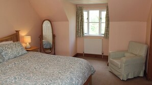Une chambre à coucher comprenant un lit, une chaise, un miroir, une fenêtre avec des rideaux et un radiateur.