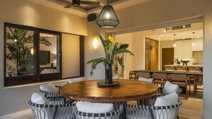 A dining area with a round wooden table surrounded by wicker chairs, a vase with flowers, and a large mirror on the wall.