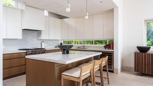 A modern kitchen with a large island, wooden cabinets, and a view of greenery outside.