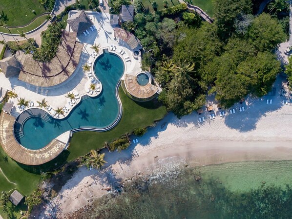 An aerial view of a resort with multiple swimming pools, a beach, and lush greenery.