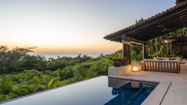 A modern infinity pool with a clear view of the ocean at sunset.