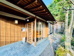 Ein traditionelles Holzhaus mit überdachter Veranda und einem Steinweg, der zu einer natürlichen Umgebung führt.