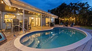 Una piscina con un porche cubierto, mobiliario exterior y vistas a palmeras.