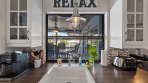 Una cocina con un lavamanos grande, una cafetera, un tostador y un letrero que dice 'RELAX'.