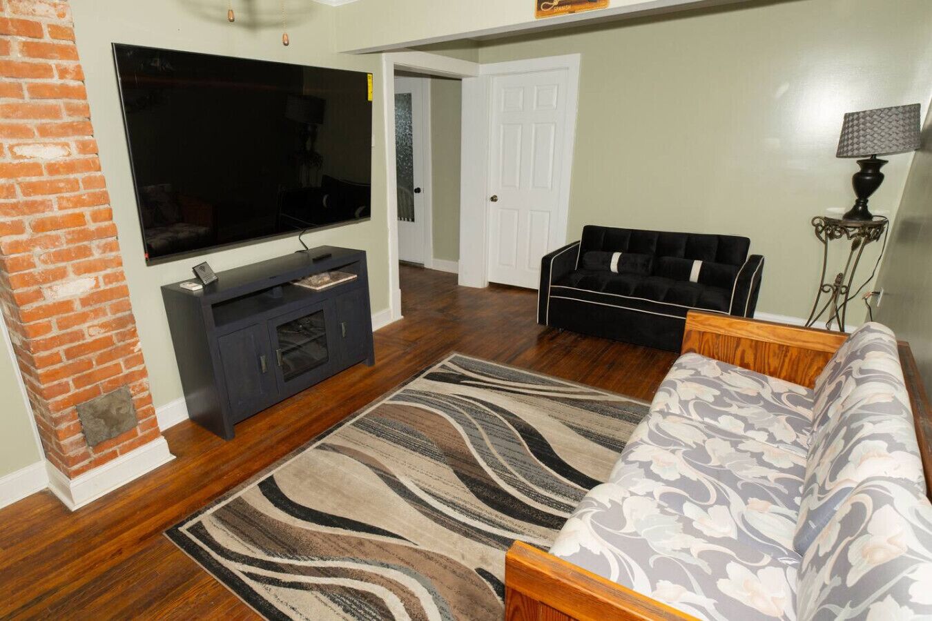 A living room with a flat-screen TV, dark entertainment unit, patterned rug, sofa, and a lamp.