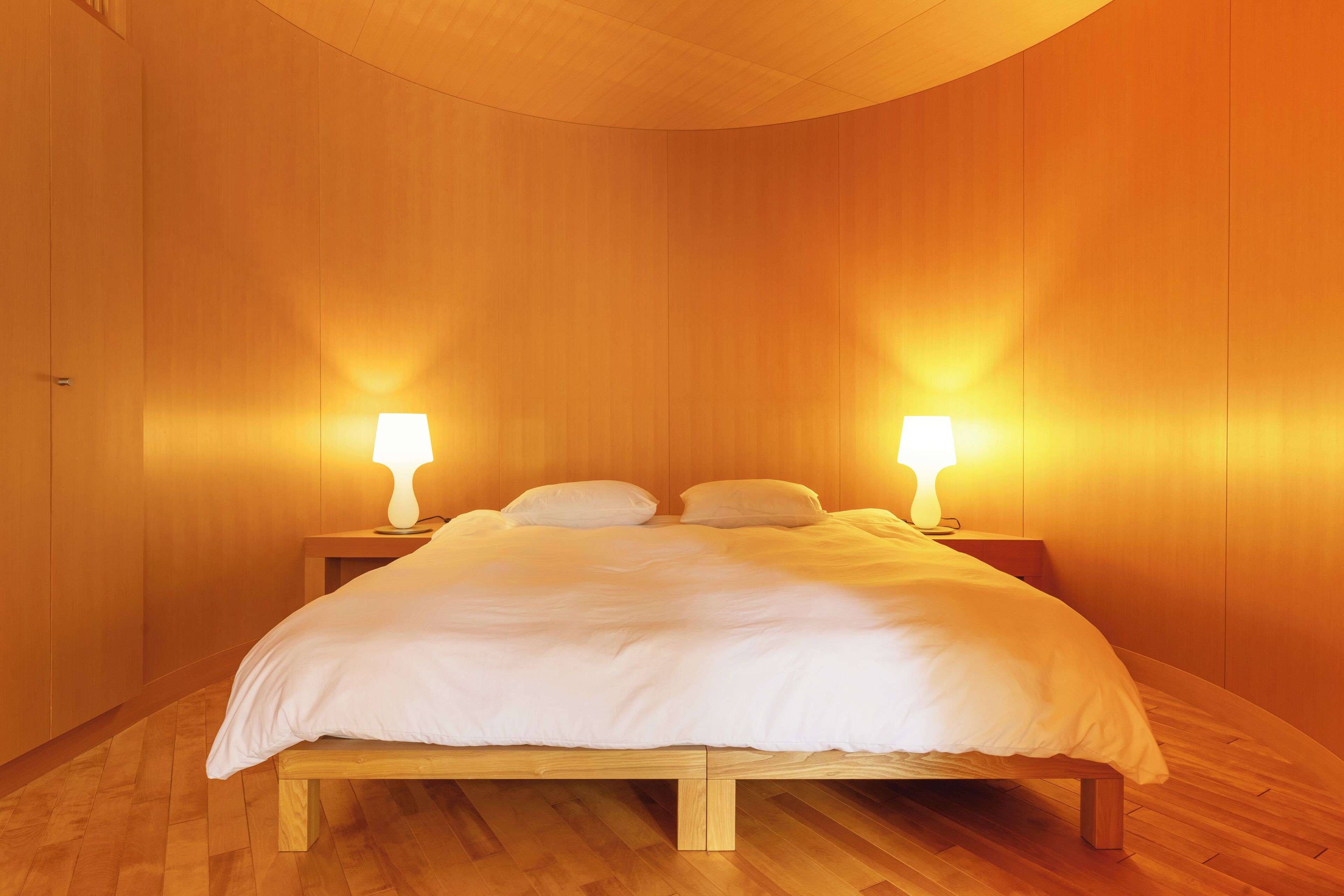 Ein ordentlich bezogenes Bett mit weißer Bettwäsche, zwei Nachttischlampen und Holzwandverkleidungen.