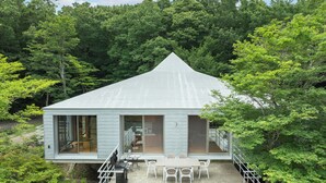 A modern house with a sloped roof, large windows, and a patio with outdoor furniture. - NASU PRIVATE FOREST (Nasu)
