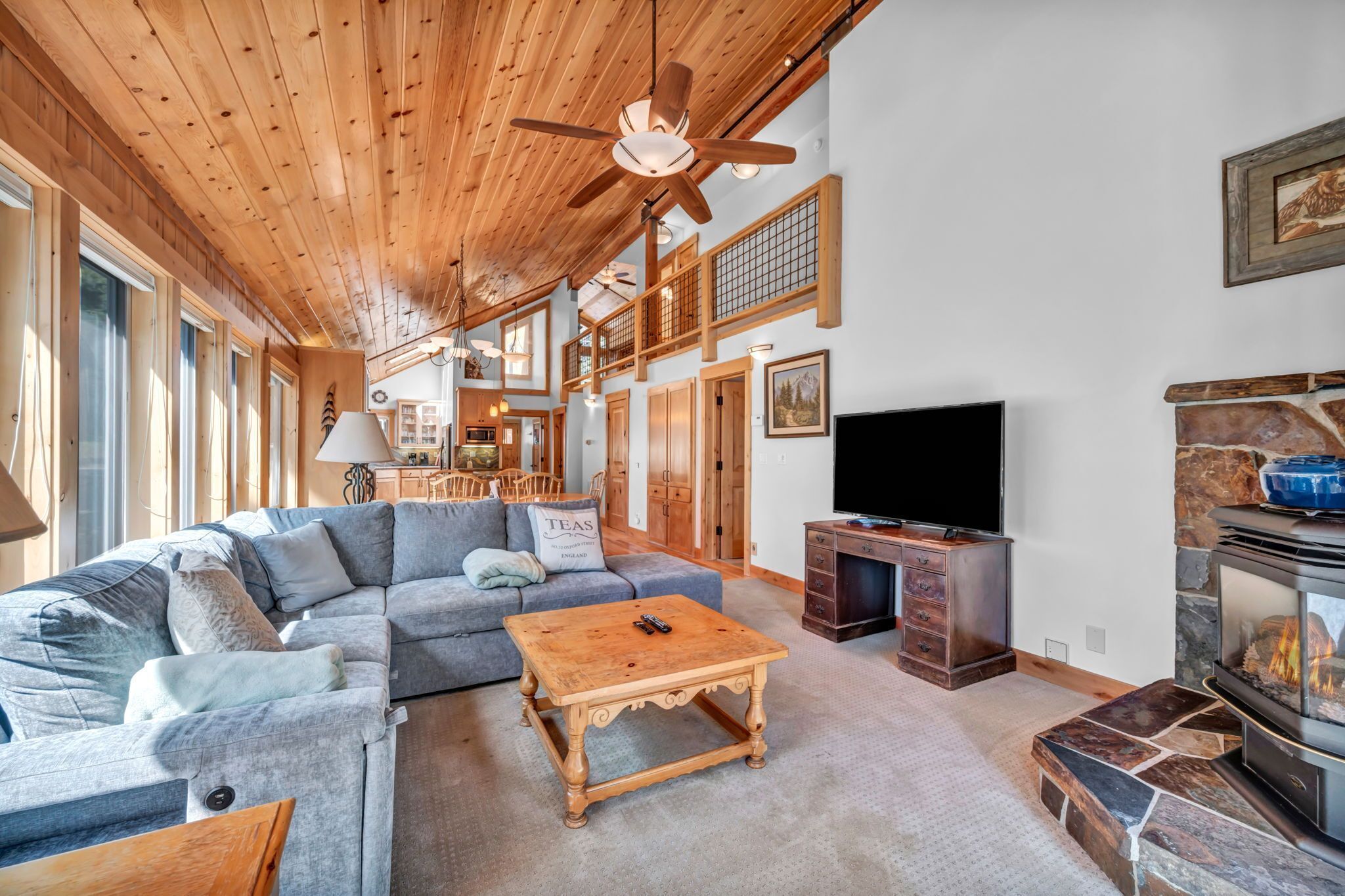 A spacious living room with a wooden ceiling, a stone fireplace, a large flat-screen TV, and a cozy seating area with a sofa and a coffee table.