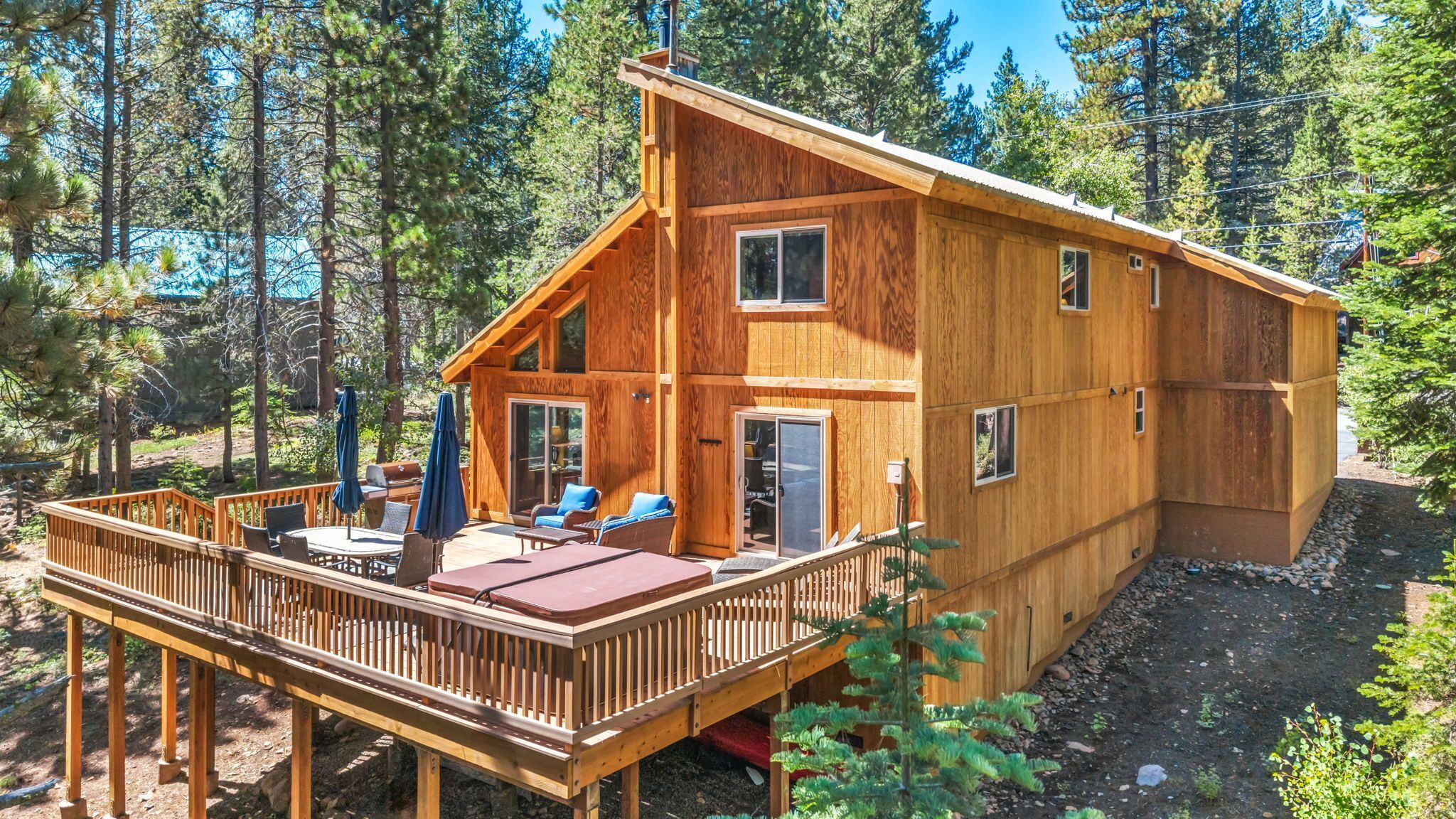 Elevated wooden deck with a hot tub and outdoor seating behind the two-story cabin.