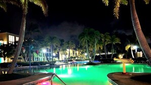 A nighttime pool area with palm trees and illuminated buildings in the background.