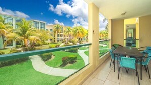 A balcony with a dining table and chairs, overlooking a well-maintained garden with palm trees and a pathway.