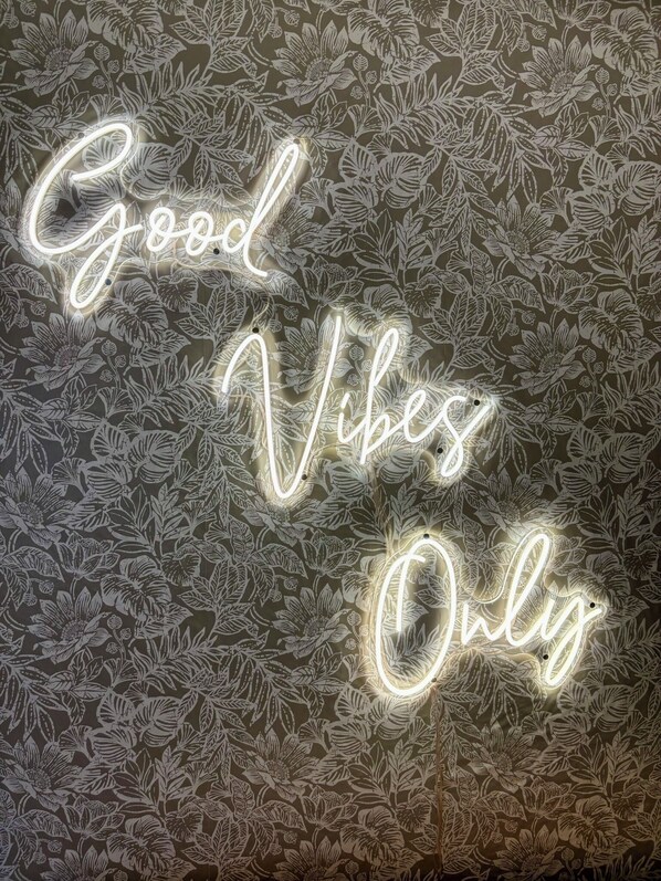 A wall with a floral pattern and a neon sign that reads 'Good Vibes Only.'