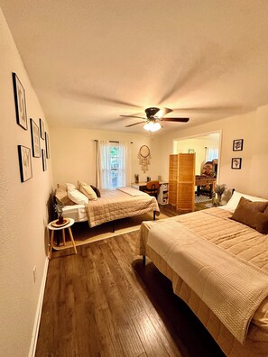 A bedroom with two beds, a ceiling fan, a desk, and a window with curtains.