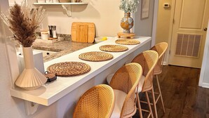 Een moderne keuken met een lange aanrecht, rieten stoelen en decoratieve objecten.
