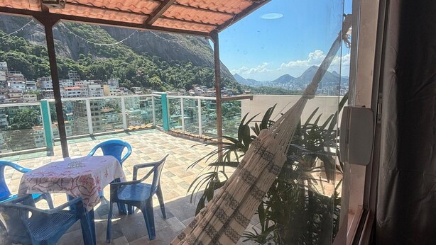 Een overdekt terras met een tafel, stoelen, een hangmat en uitzicht op een stadsbeeld en bergen.