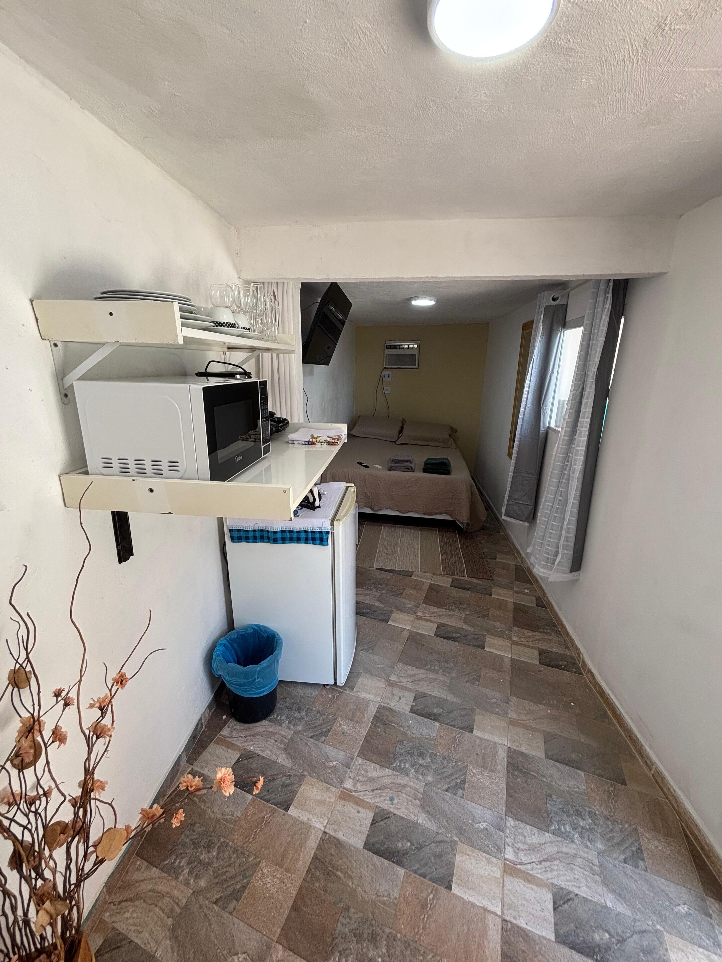 Quarto compacto com cozinha americana, uma cama e um banheiro pequeno.
