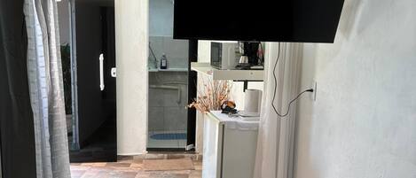 Ein Hotelzimmer mit einem Bett, einem kleinen Tisch, einem an der Wand befestigten Fernseher, einer Küchenzeile und einem durch eine offene Tür einsehbaren Badezimmer.