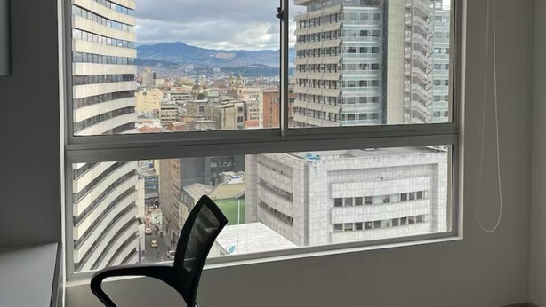 A bedroom with a large window, a black office chair, and a bed with striped bedding. - Modern studio in downtown Bogota (Bogotá)