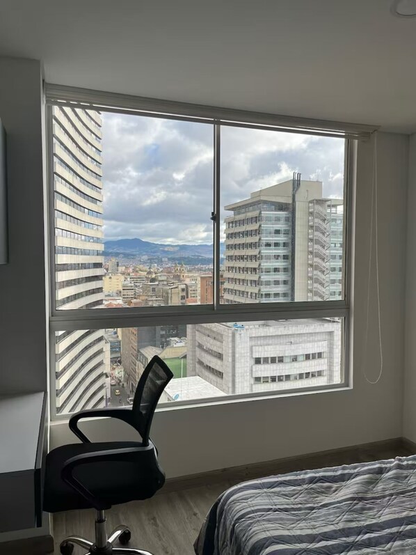 Une chambre avec une grande fenêtre, un fauteuil de bureau noir et un lit avec une literie à rayures.