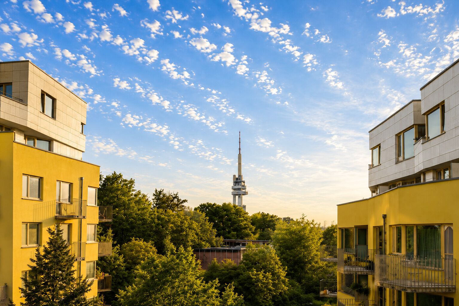 A modern building with a tower in the background, surrounded by greenery.