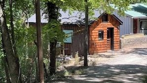 A rustic wooden cabin with a small porch and a window, surrounded by trees and a dirt path. - Happy Hideaway in our charming cabin in historic Eureka Springs with jacuzzi tub (Eureka Springs)