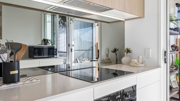 A modern kitchen with a central island, built-in appliances, and a large mirror above the countertop. - Fiano Townhouse 2 Bedrooms (Sunshine Coast)