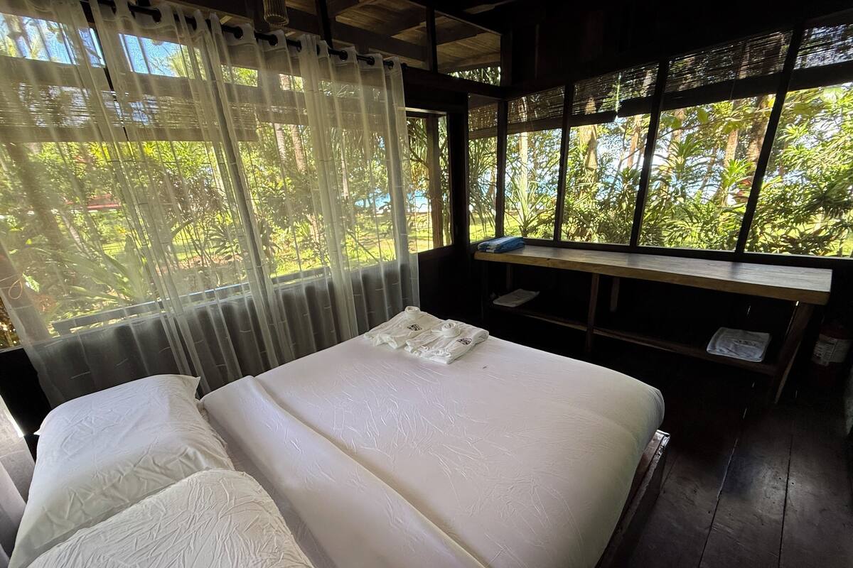 A room with a bed, a bench, and a window with a view of greenery.