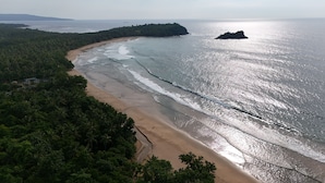 A coastal landscape with a sandy beach, a forested area, and a small island in the distance. - Kiao Beach (Puerto Princesa)