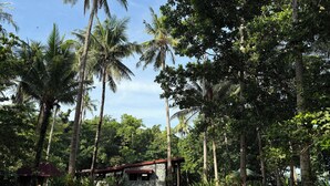 A rustic stone building with a red roof, surrounded by lush greenery and tall palm trees. - Kiao Beach (Puerto Princesa)