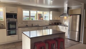 A modern kitchen with stainless steel appliances, a large island with stools, and a view through the windows. - Alpine Rose Retreat (Arrowtown)