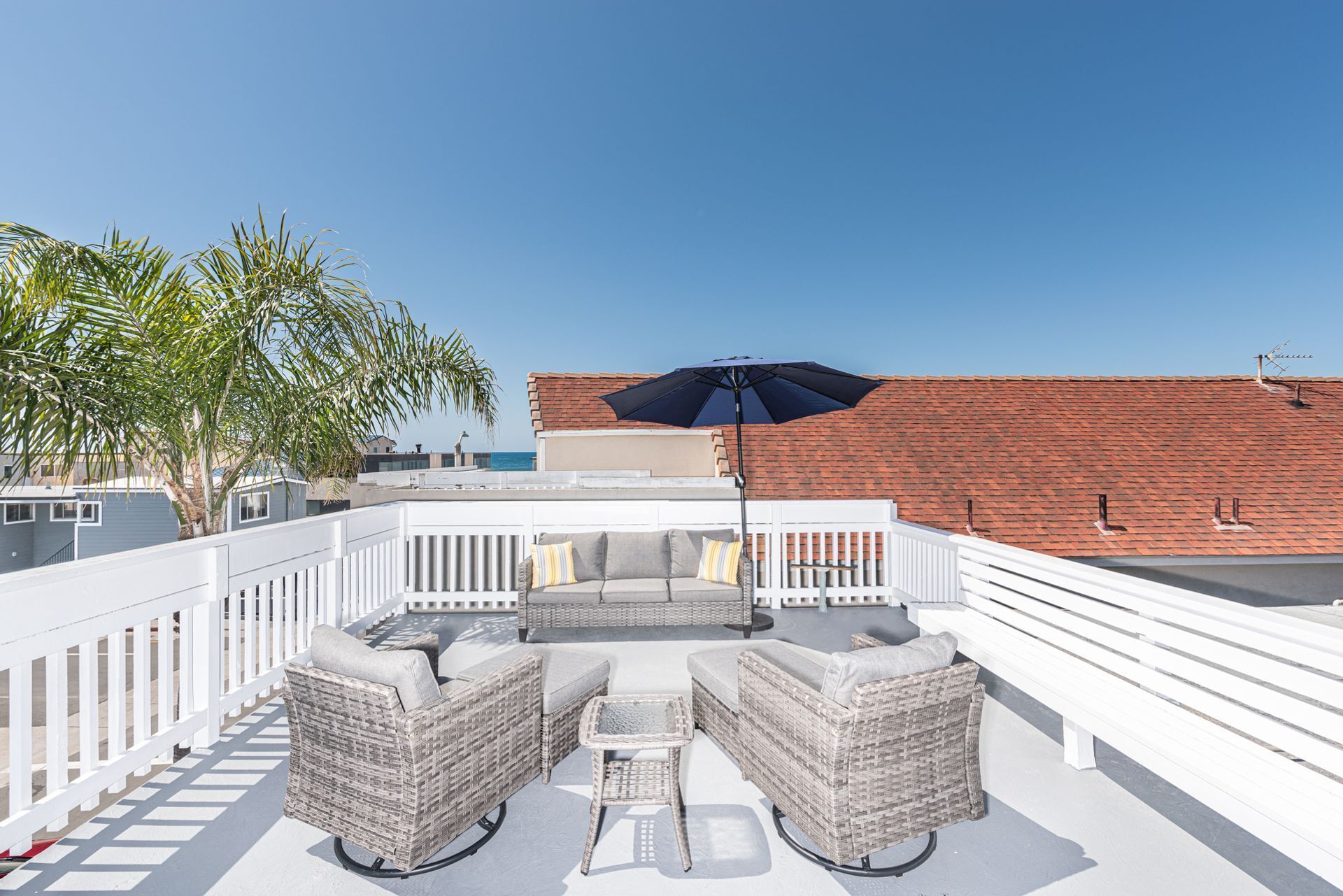 Una terraza en la azotea con muebles de mimbre, un paraguas grande y vistas al océano.