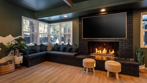 A modern living room with a large TV, a fireplace, a built-in bench, and a large window. - Summit Haven - Spa - Sauna - Gameroom - 1/4 acre backyard fenced-in (Big Bear Lake)