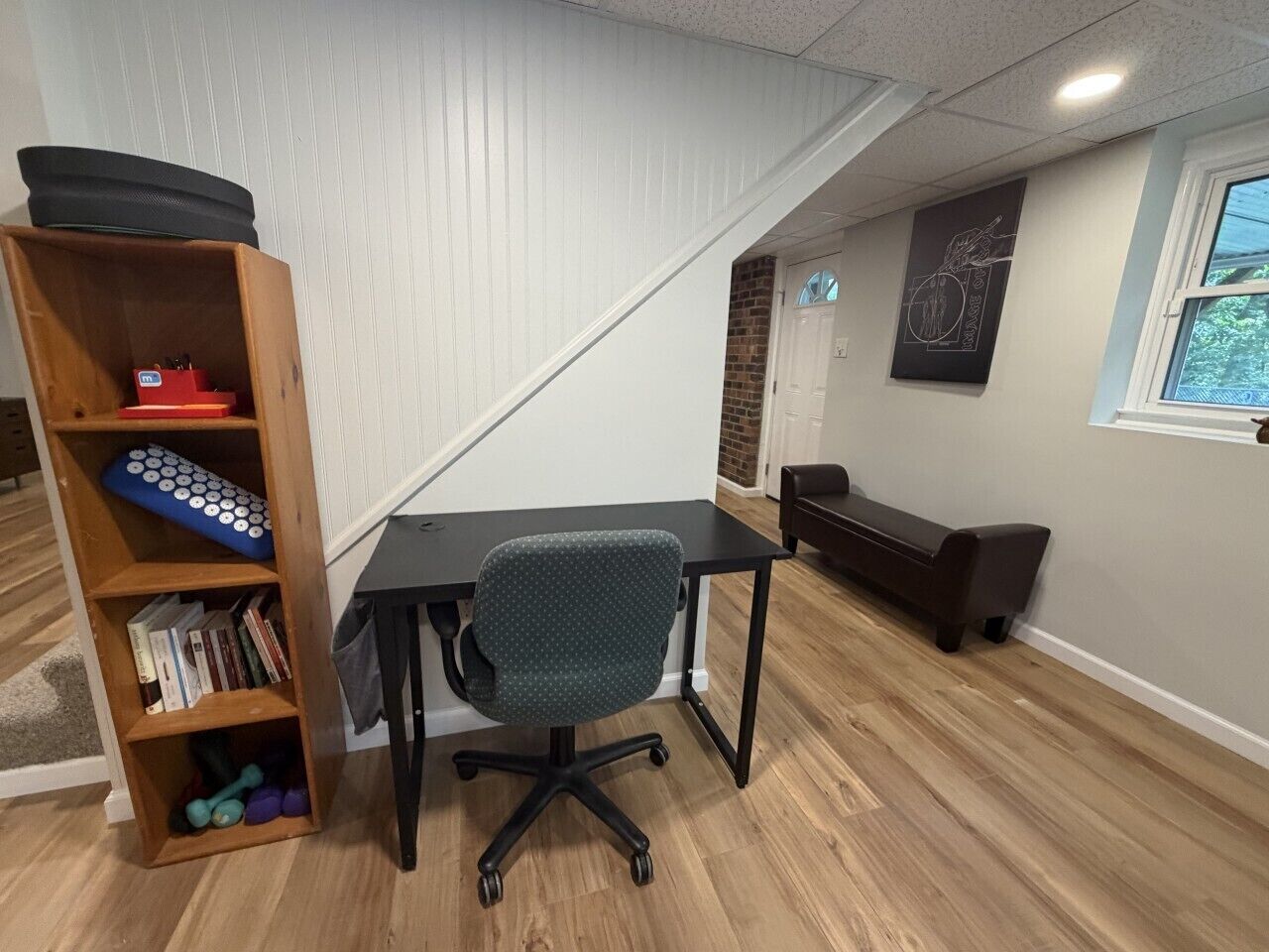 A home office with a desk, chair, bookshelf, and a bench.